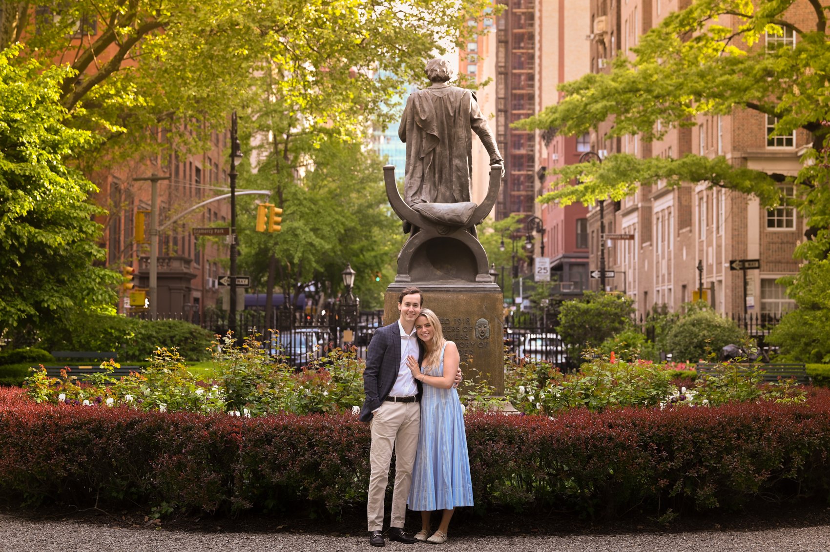 Wide shot of Kaitlin and Nick standing by a statue with the city street behind